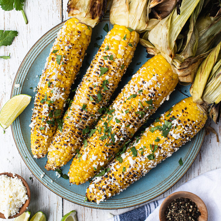 4 ears of grilled corn on the cob (Mexican Street Corn) on blue plate with husks pulled back