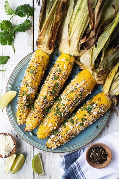 4 ears of grilled Mexican Street Corn with husks on blue plate