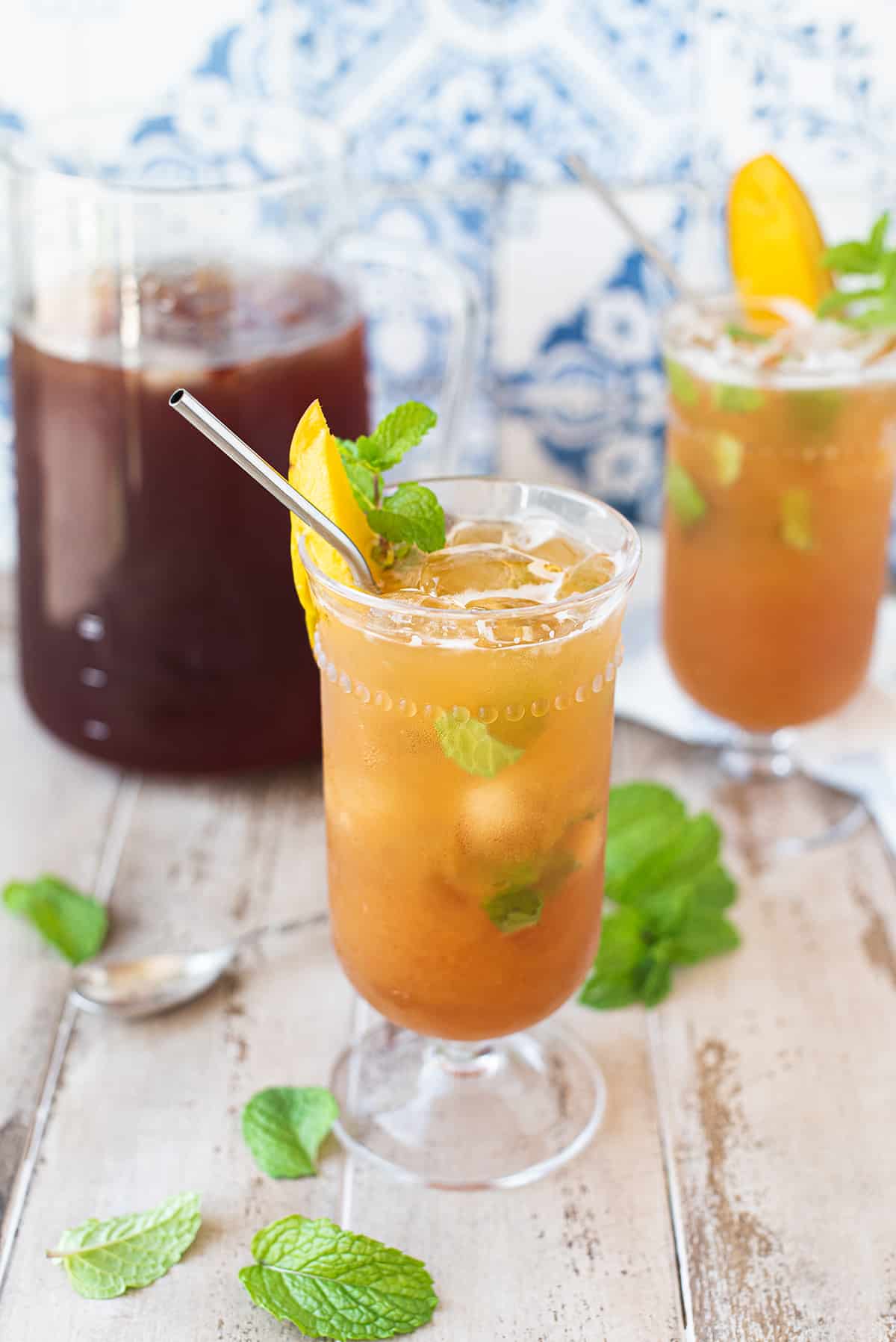 twisted iced tea cocktail with straw, garnished with mint + mango slice