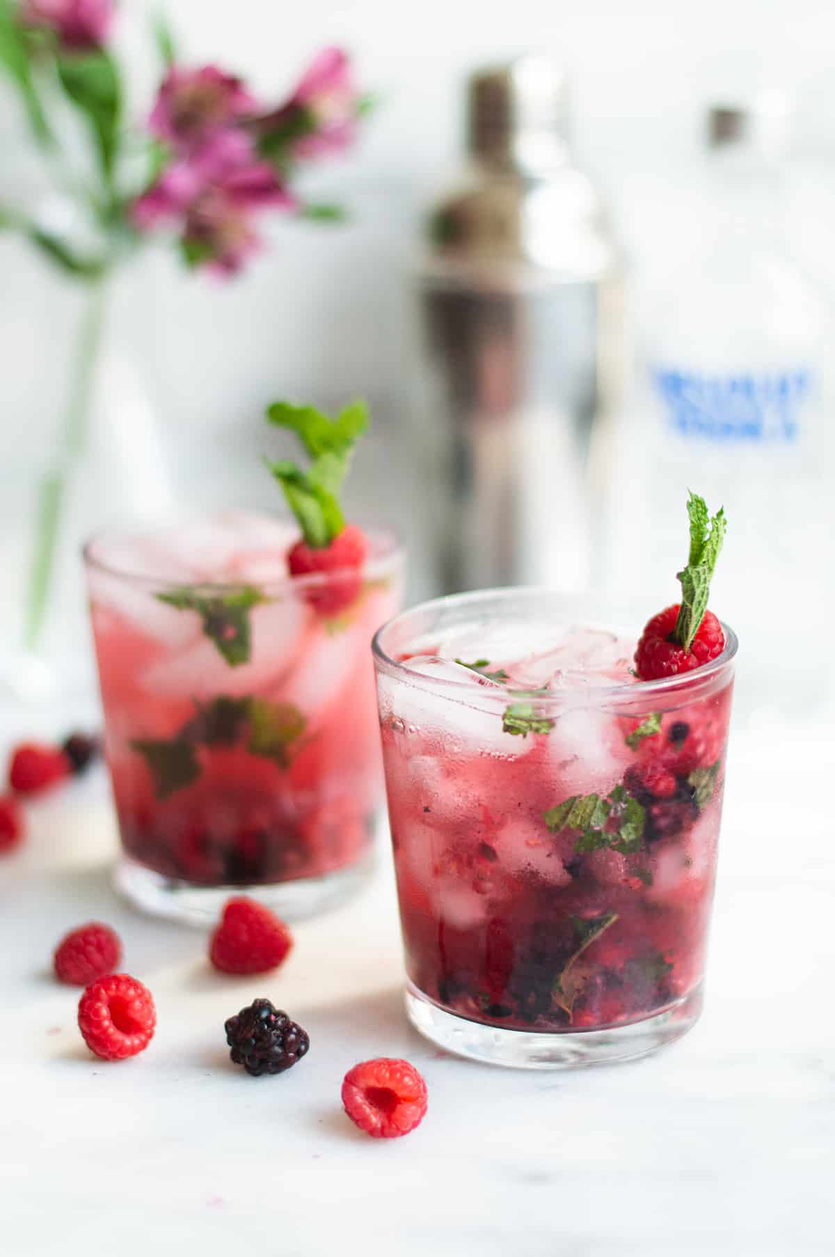 2 raspberry mojitos on marble counter, garnished with mint and berries.