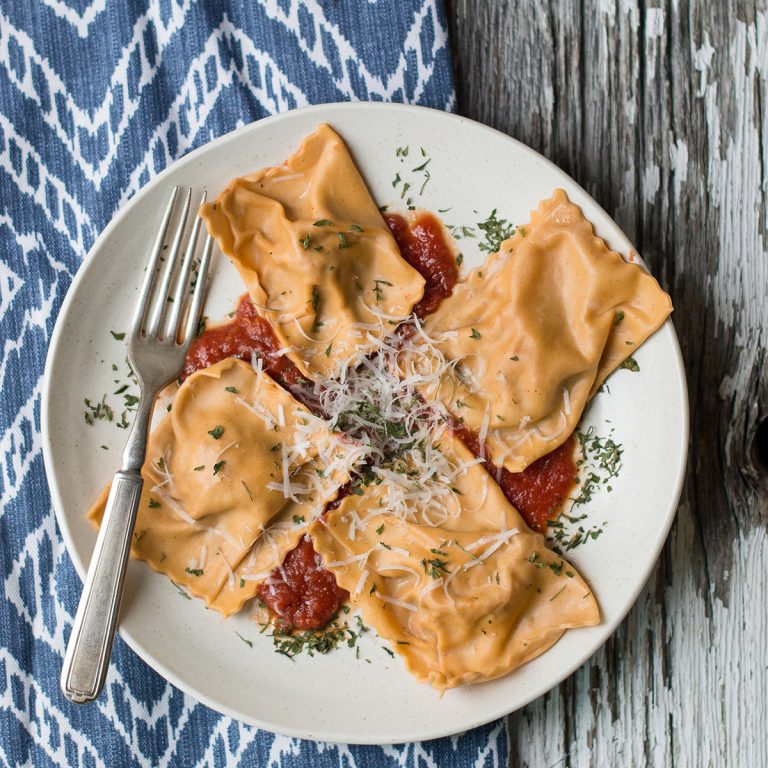 4 raviolis on white plate with fork + blue patterned napkin