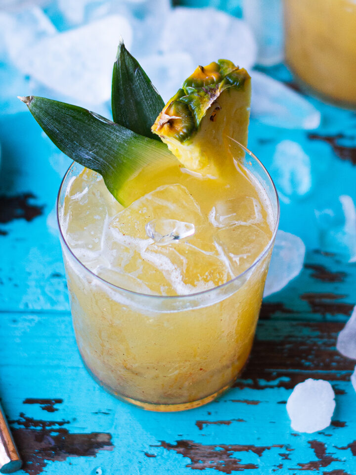 pineapple cocktail on blue table garnished with fresh pineapple