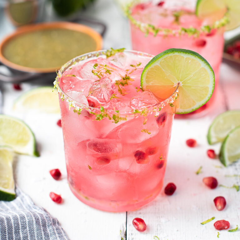 pink margarita in glass, garnished with lime + pomegranate seeds