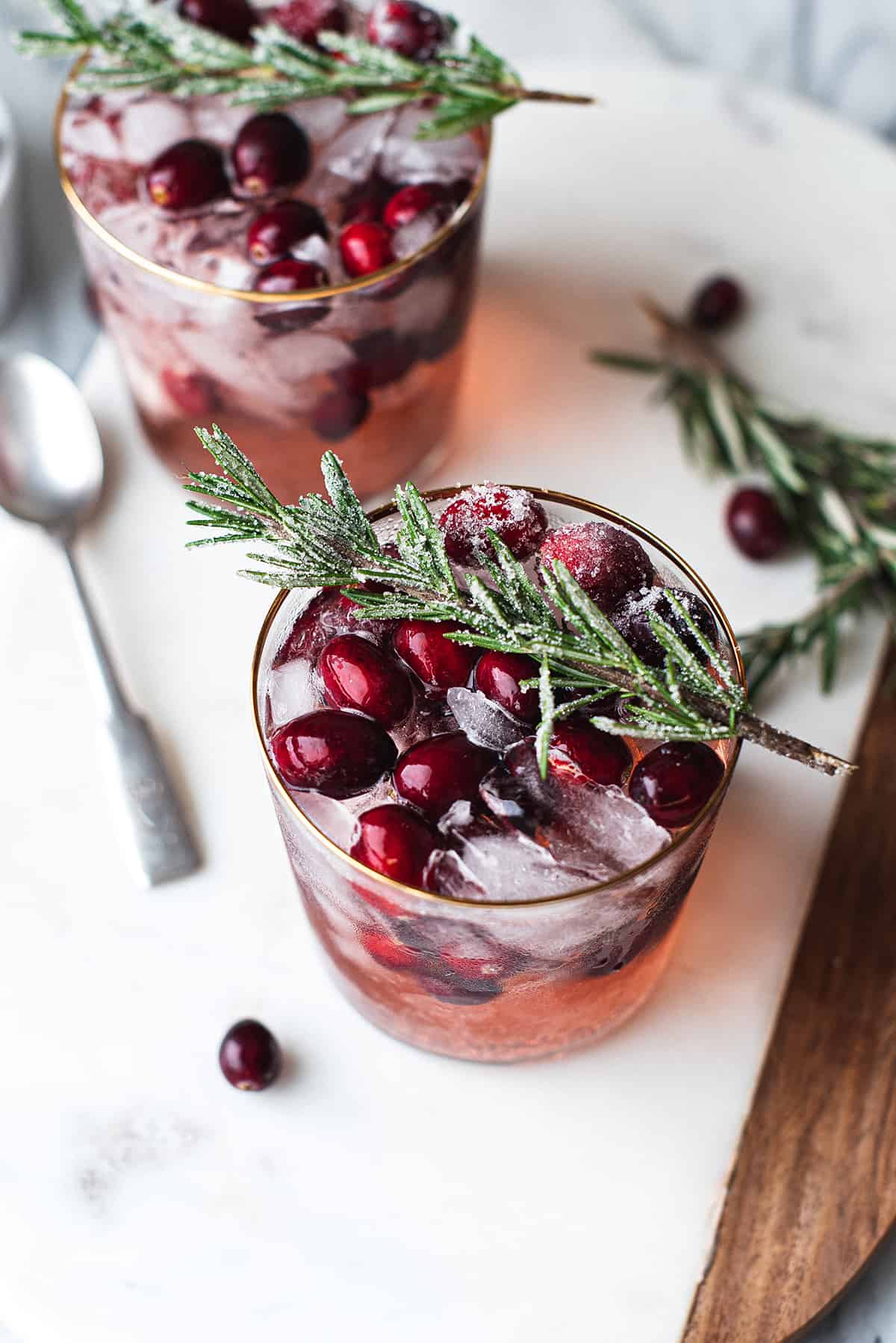 vodka cocktail with cranberries in glass, garnished with sugar covered rosemary