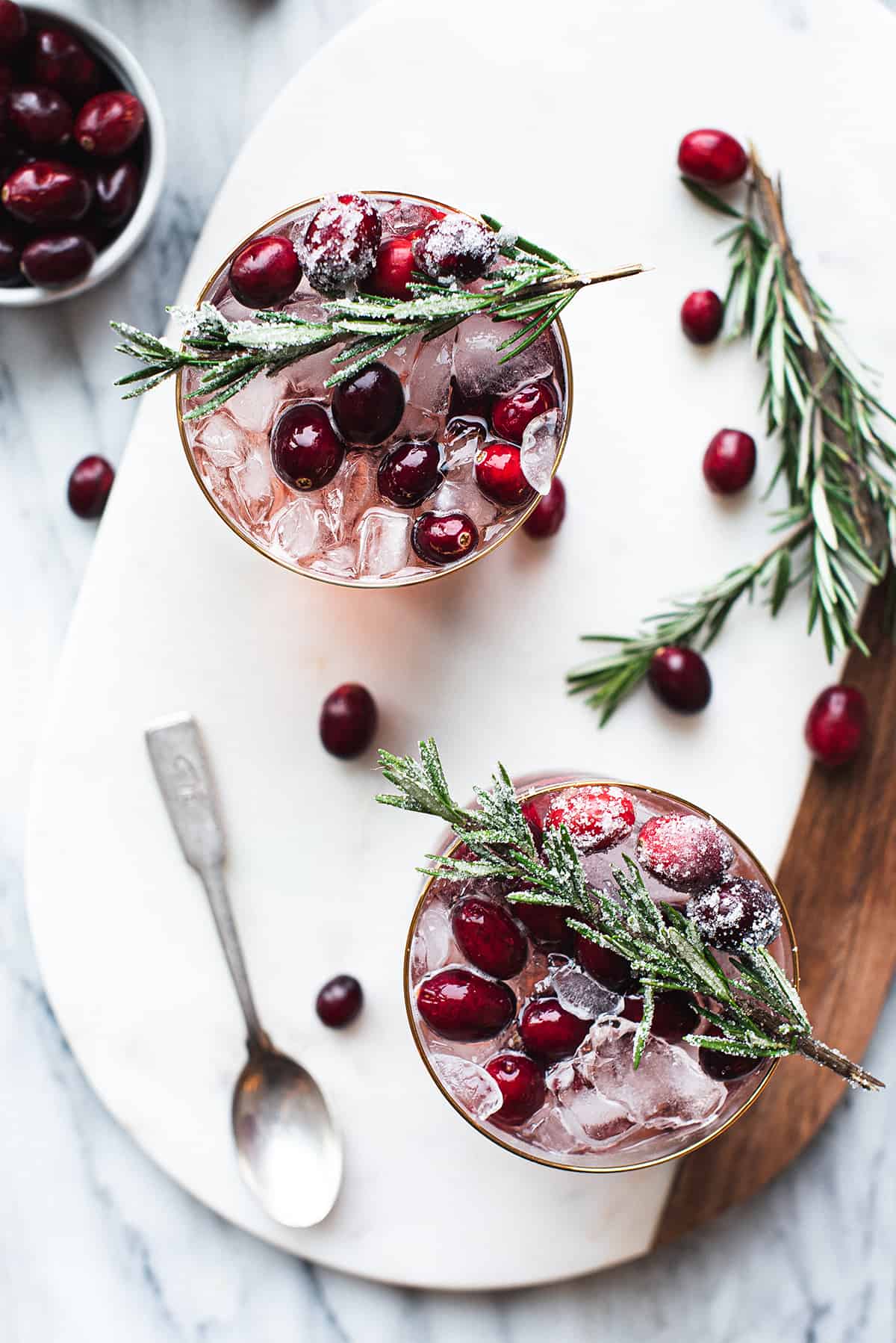 2 cranberry cocktails with rosemary garnish, cranberries & spoon