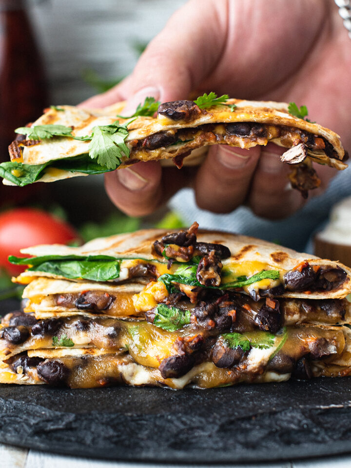 stack of quesadillas on black platter, with hand grabbing one