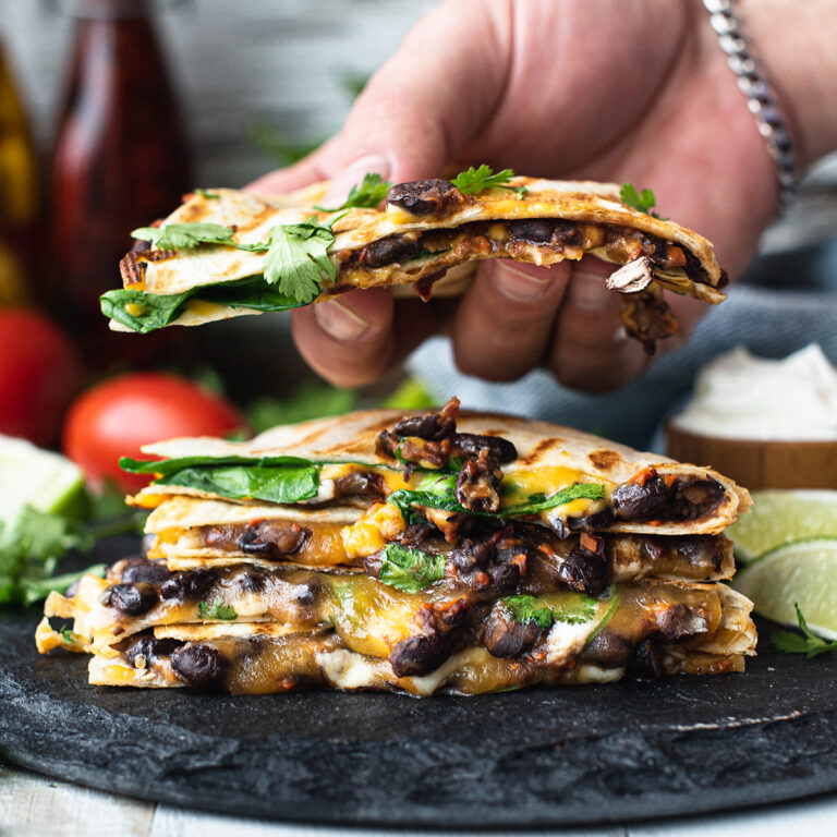stack of quesadillas on black platter, with hand grabbing one