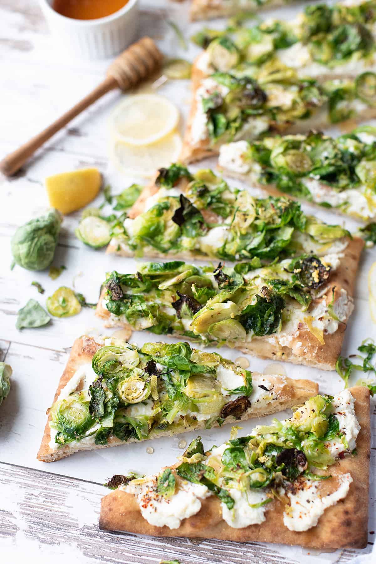 slices of brussels sprouts flatbread on white table with honey dripper