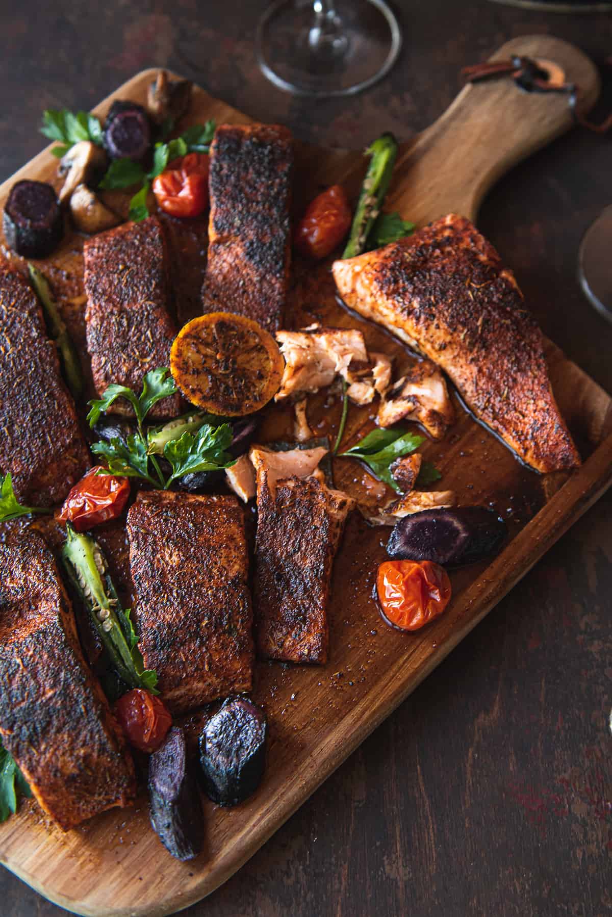 blackened salmon pieces, cut on wooden serving board and garnished with lemon halves, tomatoes, and greens