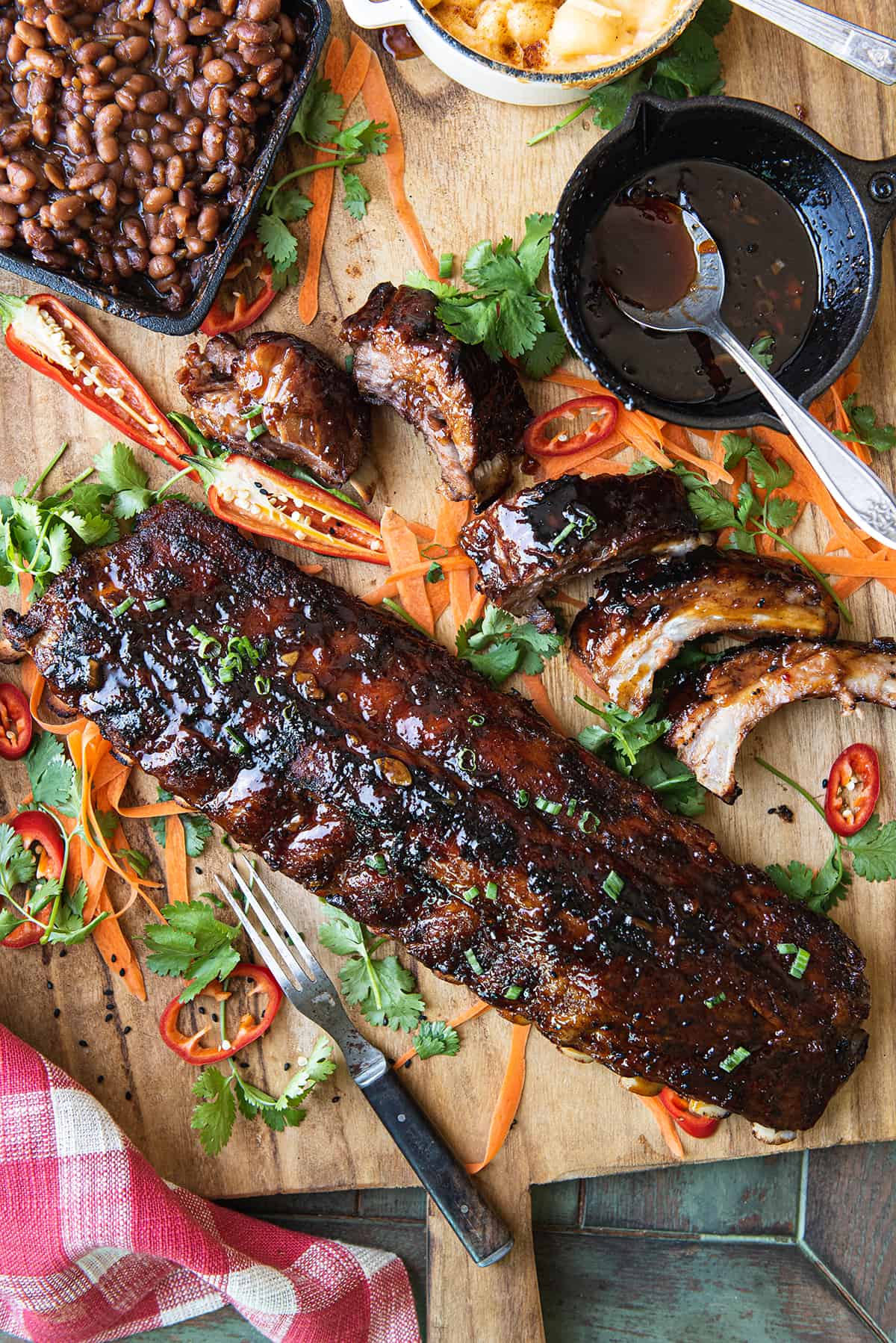 rack of baby back ribs on wooden platter with carrots, greens, barbecue sauce