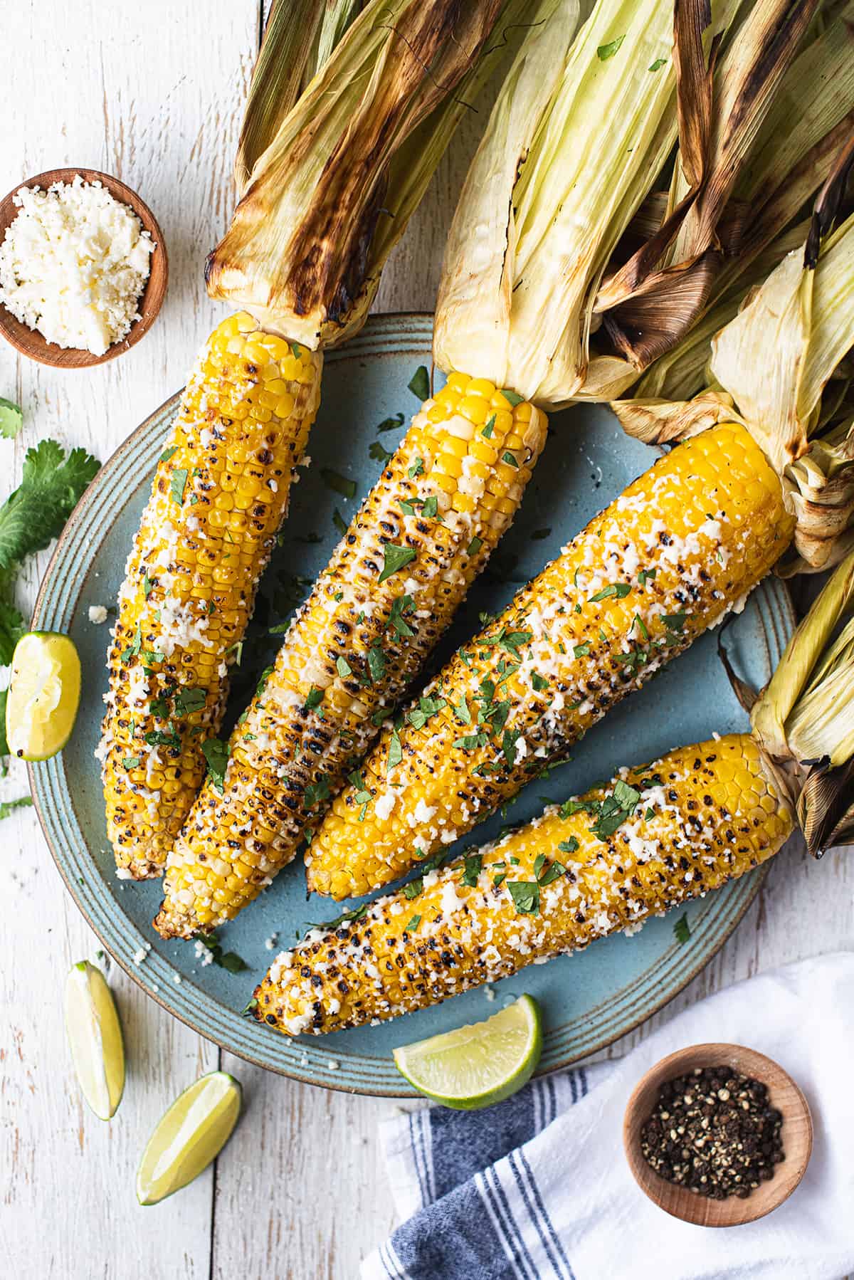 4 ears of grilled corn on the cob (Mexican Street Corn) with husks pulled back on blue plate