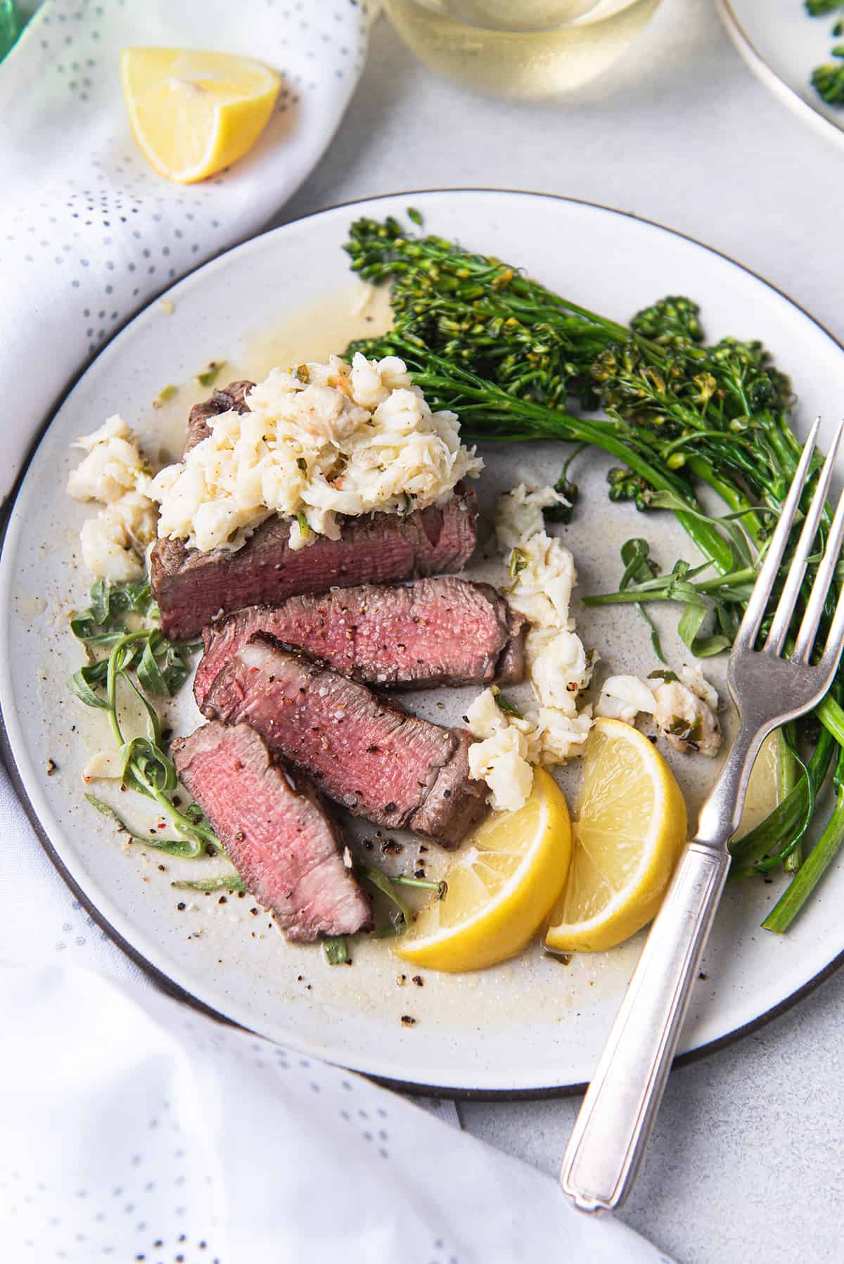 grilled filet slices on white plate, topped with crab meat + broccolini and fork