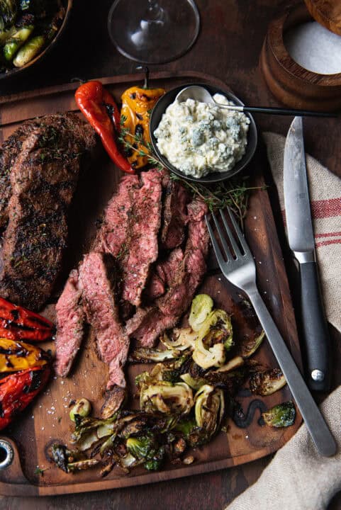 flat iron steaks, sliced on wooden board with brussels sprouts, peppers, blue cheese, fork & knife