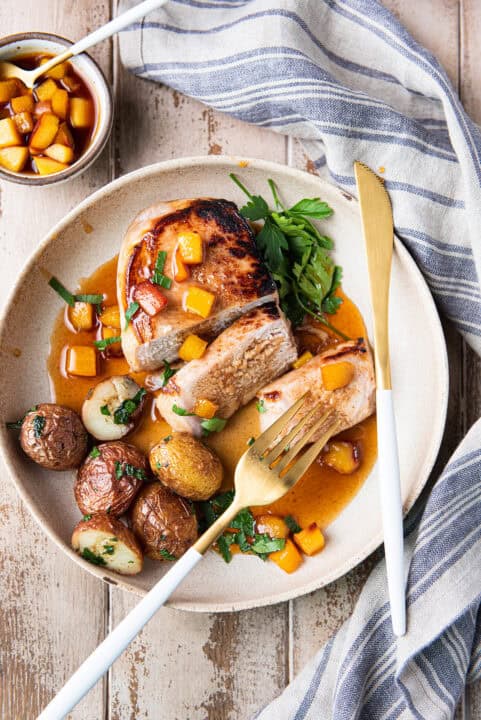 slice pork chop with peach marinade on white plate with potatoes + knife & fork