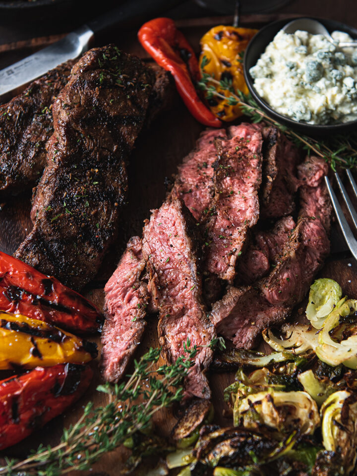 flat iron steak, sliced on wooden platter with fork + vegetables