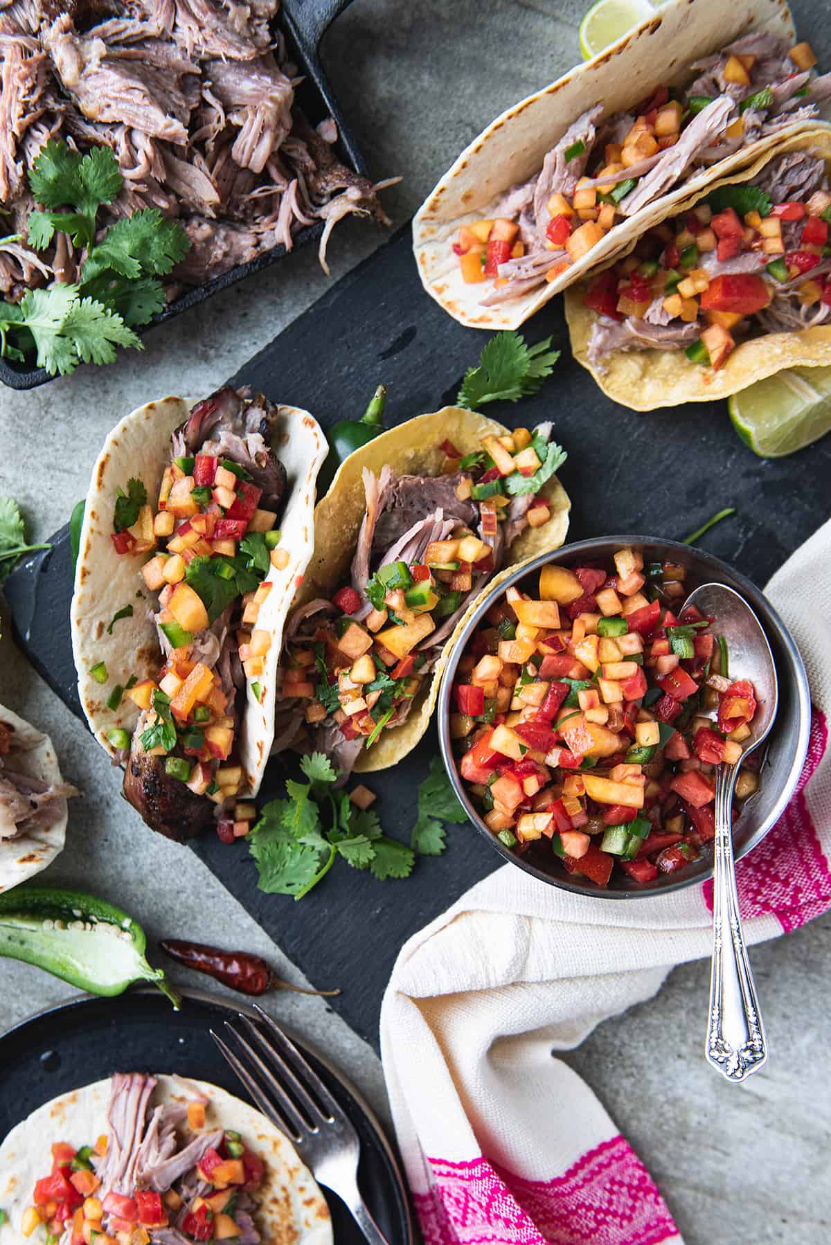 two pork tacos on black board with bowl of peach salsa