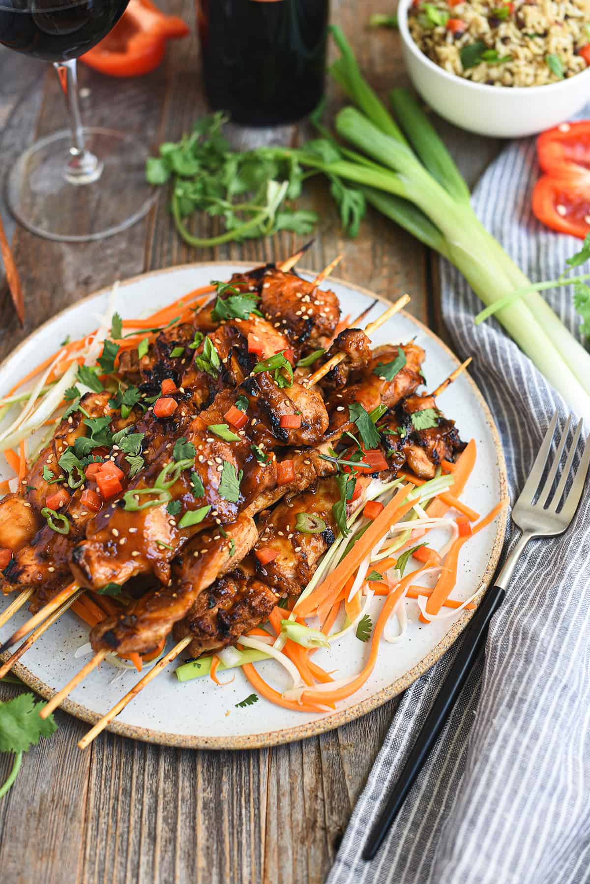Asian BBQ chicken skewers piled on white ceramic plate with fork and blue napkin