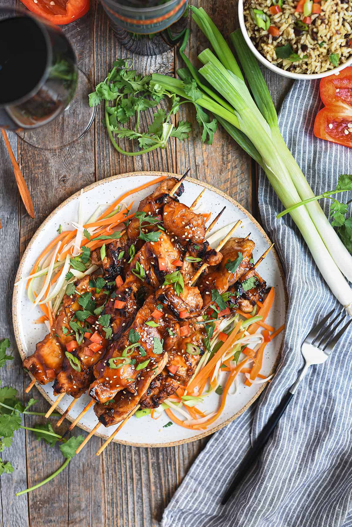 Asian BBQ chicken skewers piled on white ceramic plate with fork, blue napkin, and greens