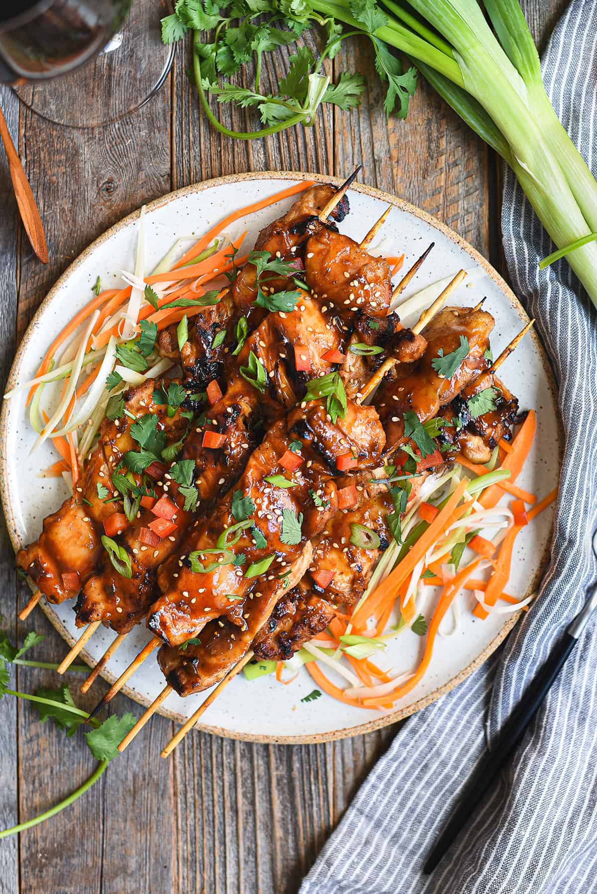 Asian BBQ chicken skewers piled on white ceramic plate with fork, blue napkin, and greens