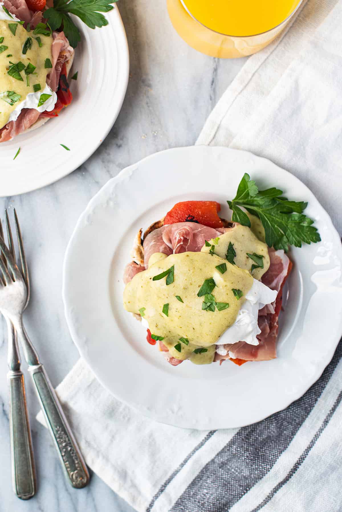 Italian Eggs Benedict served on white plate drizzled with Hollandaise sauce + fork