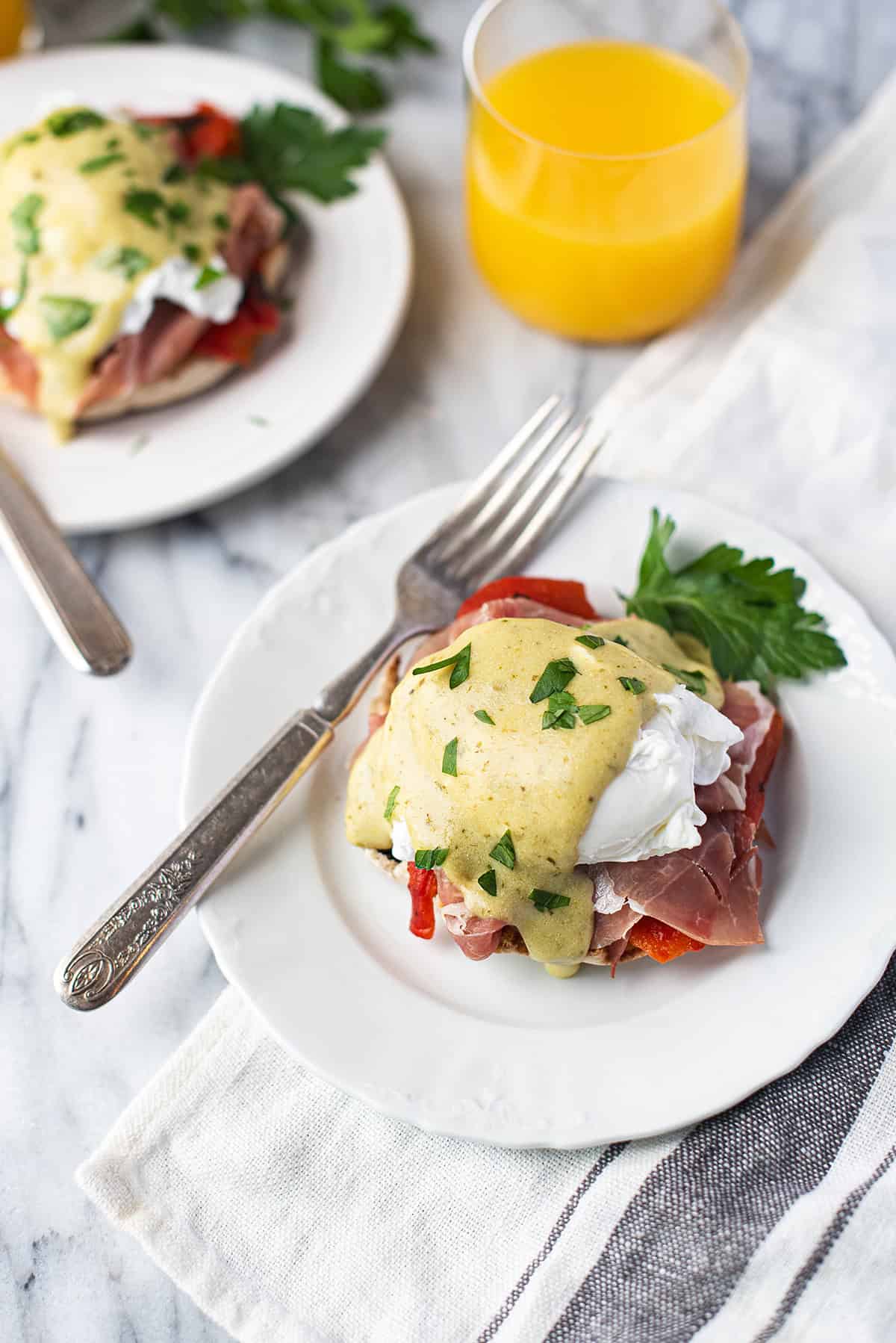 Italian Eggs Benedict served on white plate drizzled with Hollandaise sauce + fork