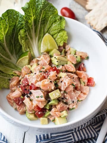 salmon ceviche in white bowl, garnished with lettuce leaf + blue striped napkin