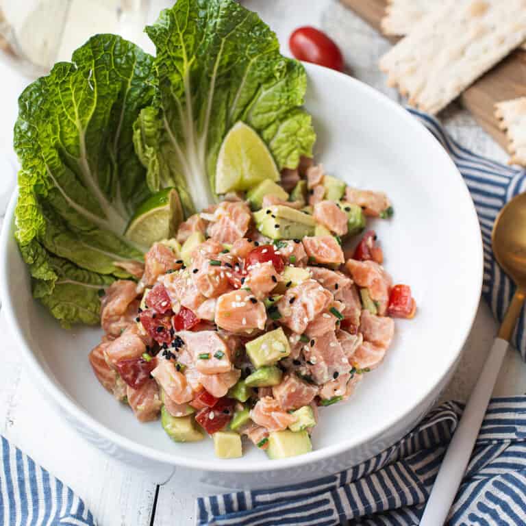 salmon ceviche in white bowl, garnished with lettuce leaf + blue striped napkin