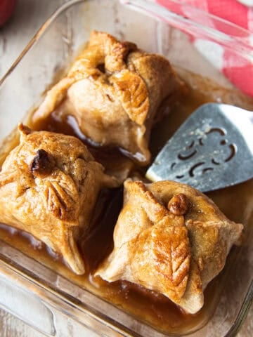 3 apple dumplings in baking dish with pie server + red checked napkin