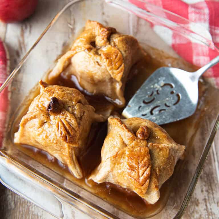 3 apple dumplings in baking dish with pie server + red checked napkin