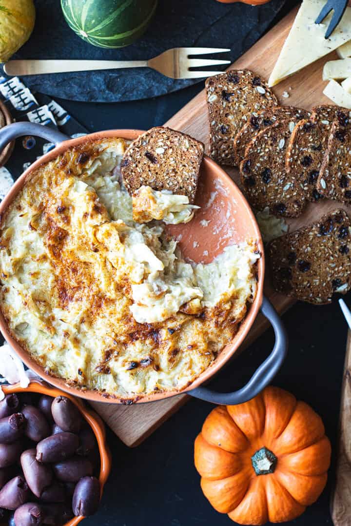 Baked artichoke dip with golden broiled top served in an orange baking dish with crusty bread for dipping