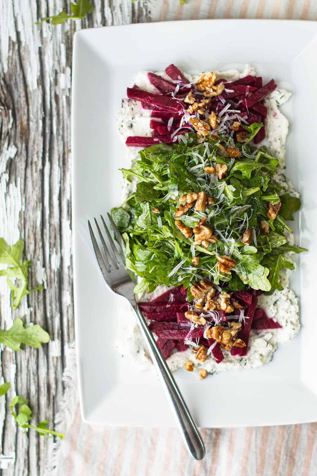 arugula and beet salad plated on a bed of herbed ricotta with toasted walnuts and grated parmesan on a white rectangular platter