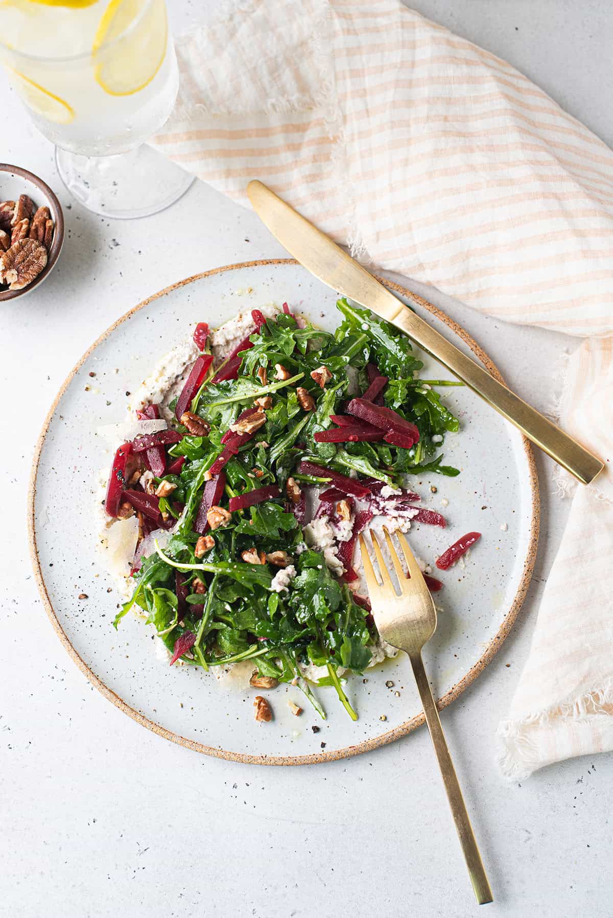 close up of arugula beet salad with herbed ricotta and julienned beets on a speckled ceramic plate with gold fork and knife