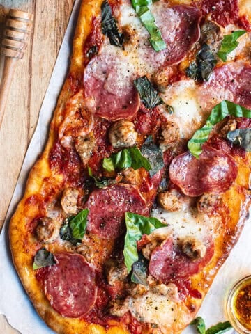 A pizza with meat, cheese and basil on a wooden cutting board.