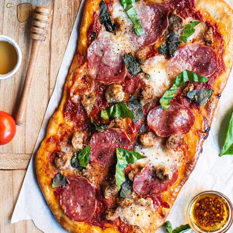 A pizza with meat, cheese and basil on a wooden cutting board.