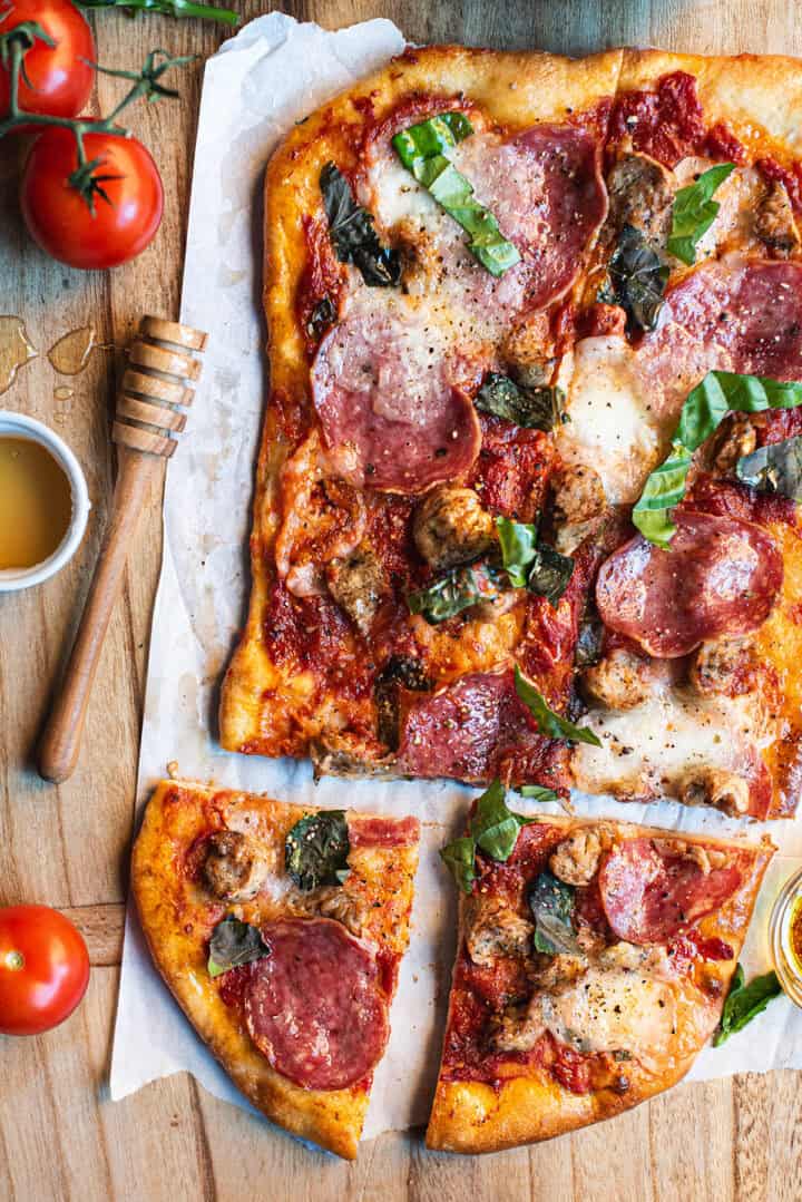A pizza with meat, cheese and tomatoes on a cutting board.