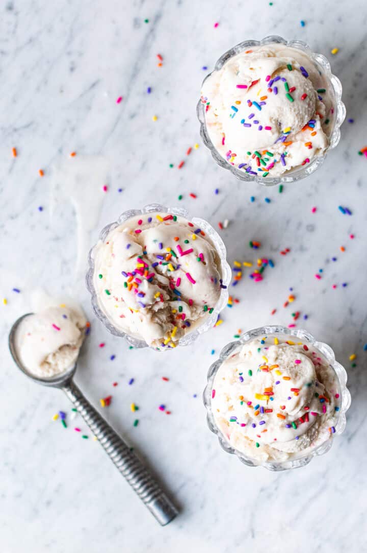 three glass bowls of birthday cake ice cream with sprinkles and ice cream scoop