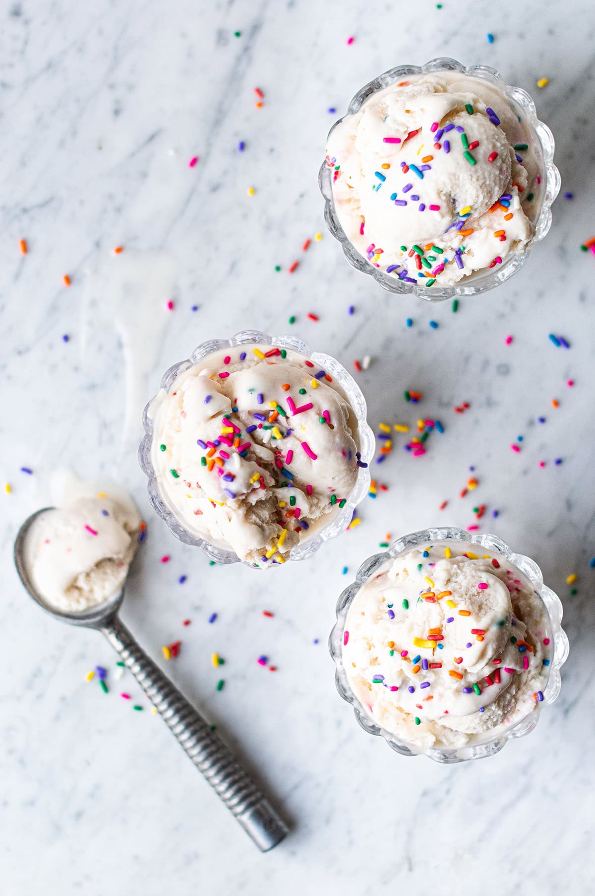 three glass bowls of birthday cake ice cream with sprinkles and ice cream scoop