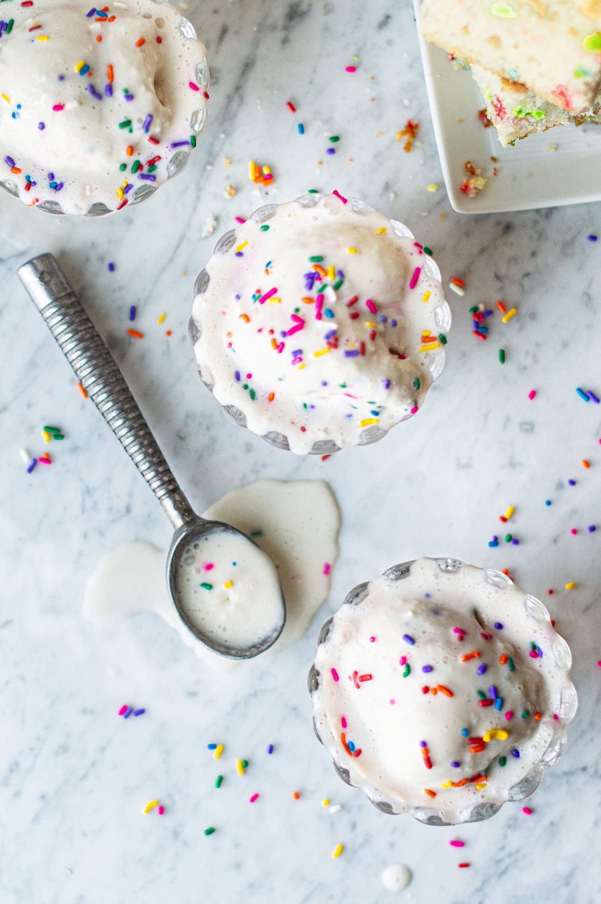 overhead shot of three bowls of birthday cake ice cream with melted scoops and sprinkles