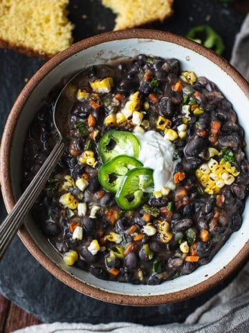 bowl of black bean soup with spoon, topped with pepper slices and sour cream