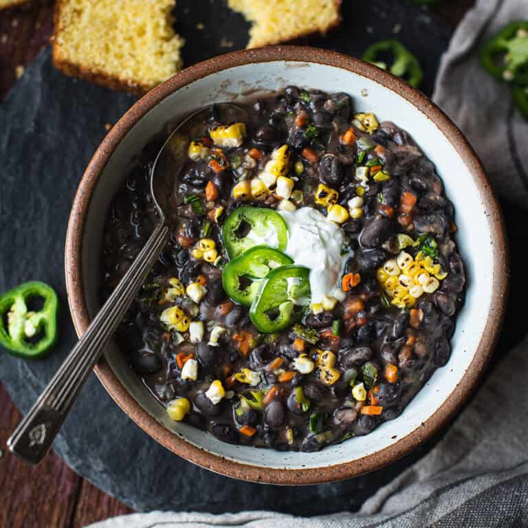 bowl of black bean soup with spoon, topped with pepper slices and sour cream