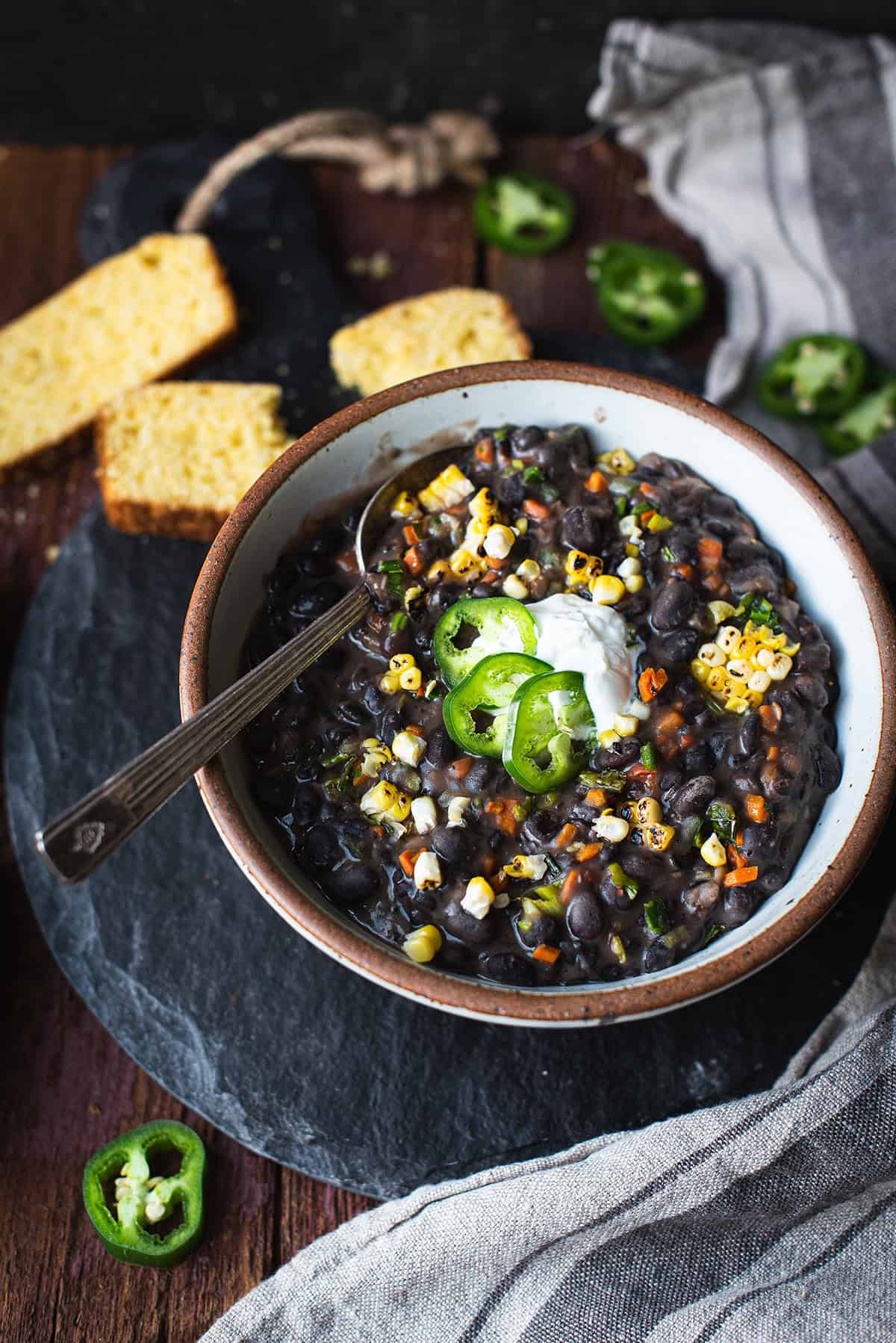 bowl of black bean soup with spoon topped with sour cream and sliced peppers