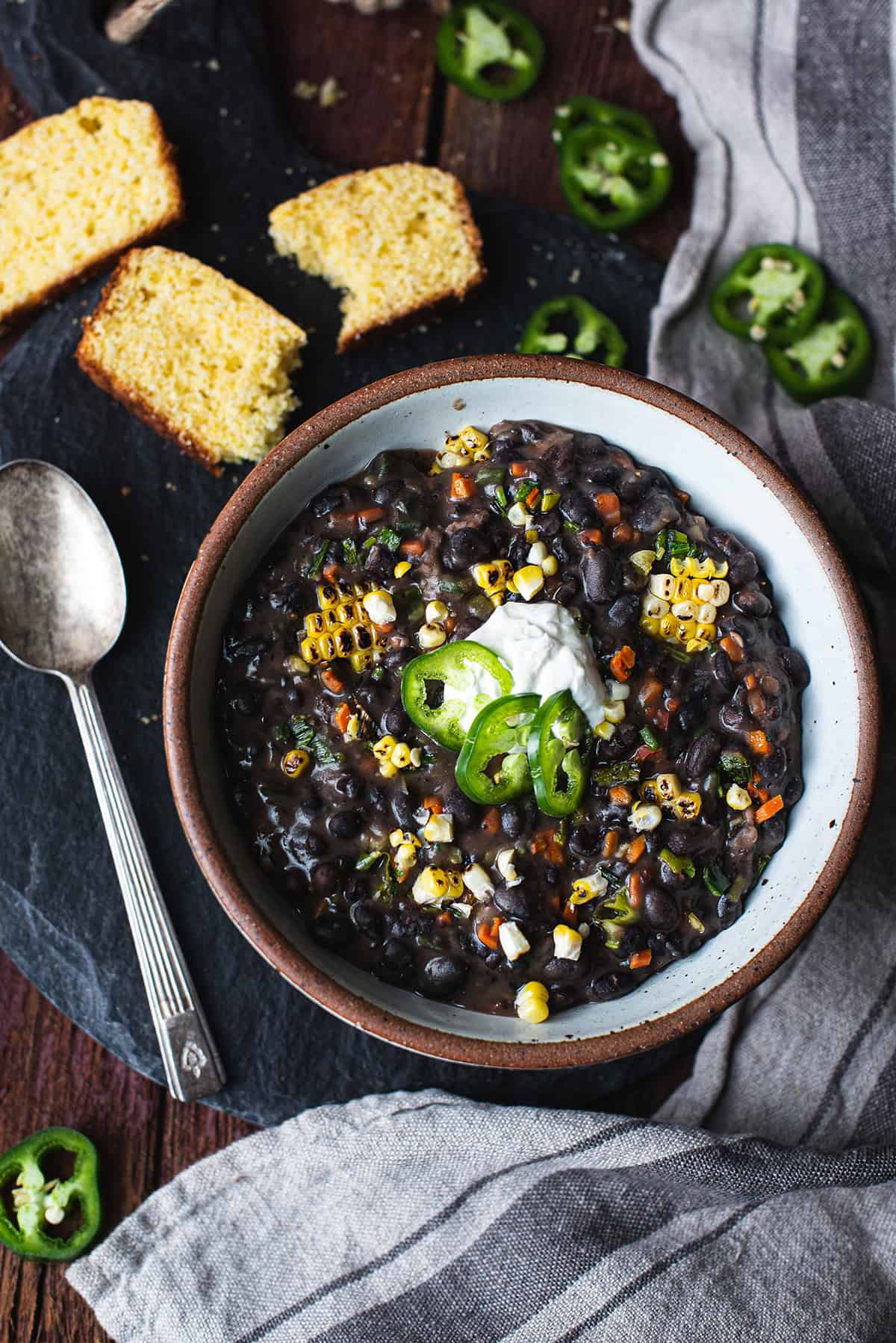 bowl of fire roasted black bean soup on platter with spoon, topped with sliced peppers and sour cream