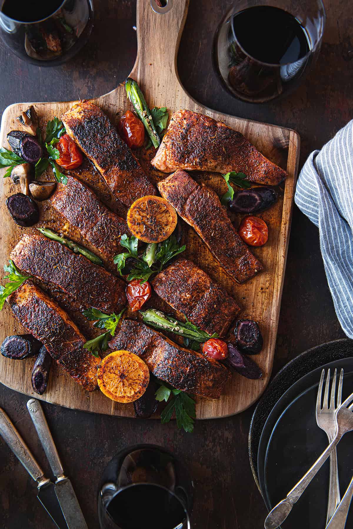 blackened salmon filets, served on wooden board, garnished with lemons, tomatoes, & greens