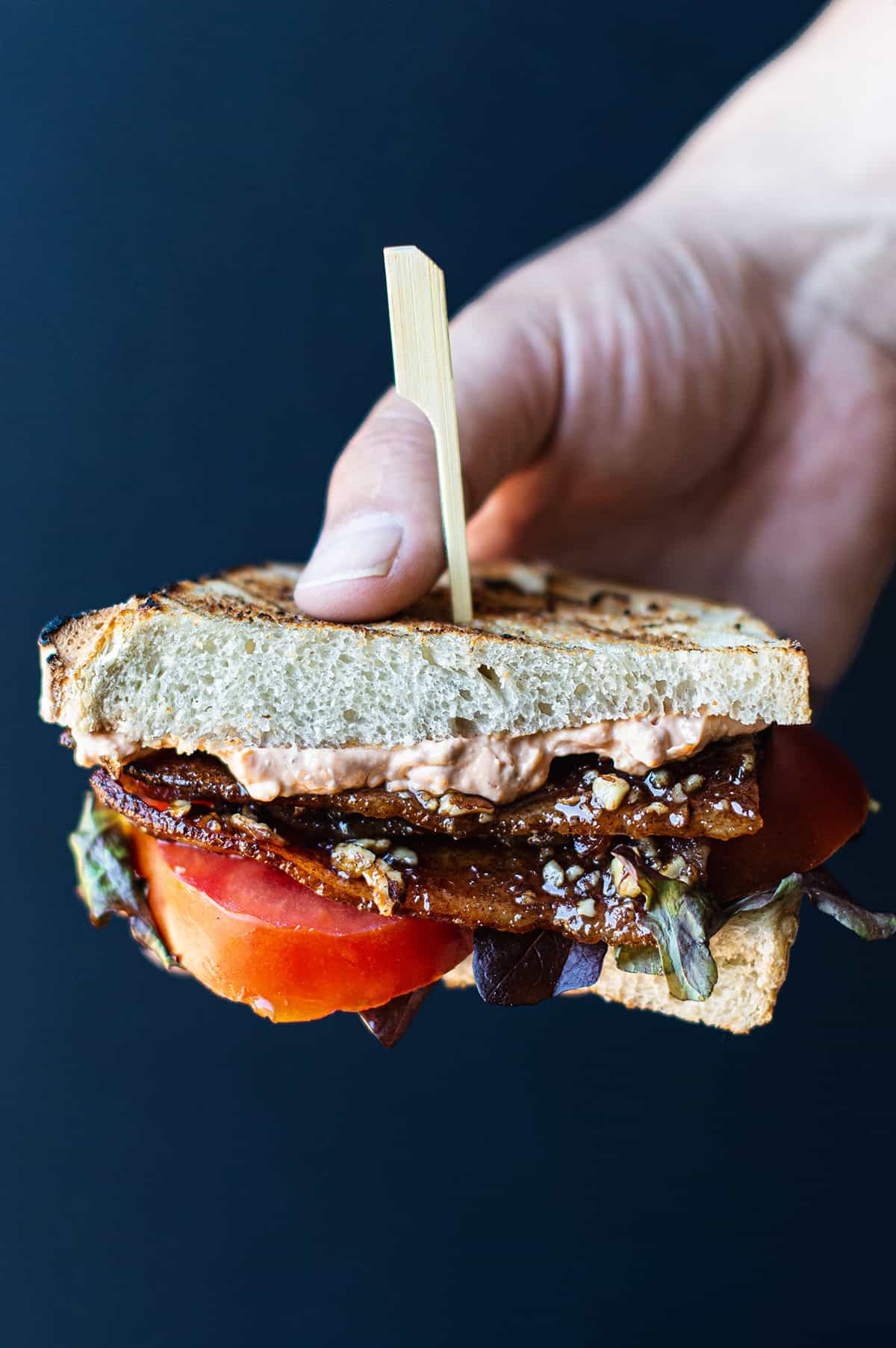 hand holding a BLT sandwich half on grilled sourdough with Sriracha aioli