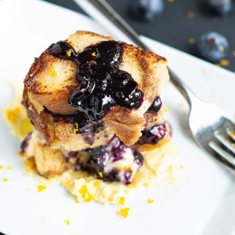 Italian bread pudding topped blueberry compote on white plate with fork