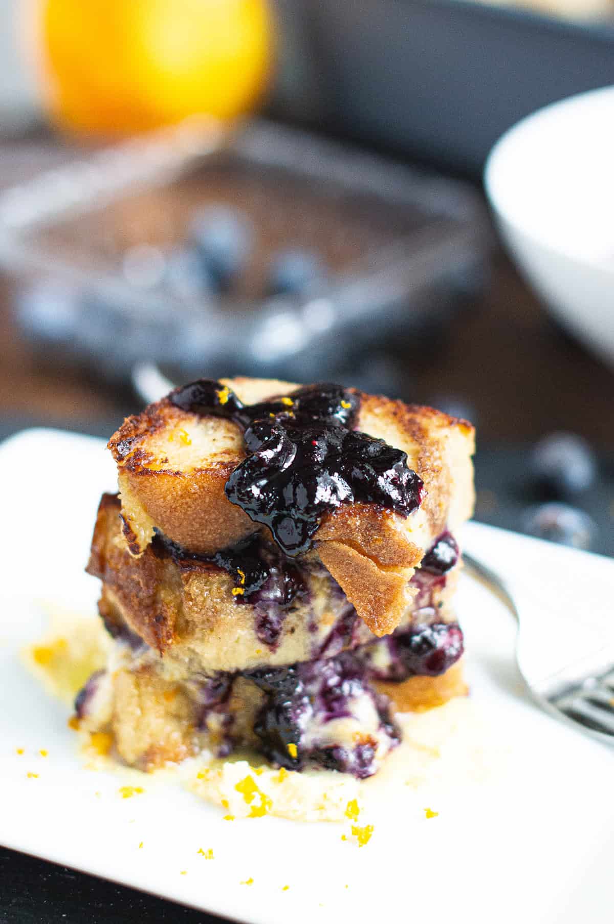 Italian bread pudding topped blueberry compote on white plate with fork