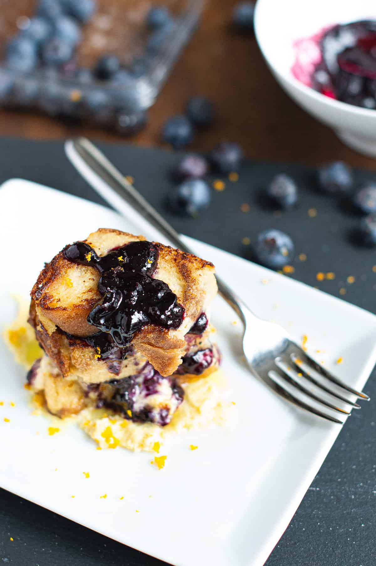 Italian bread pudding topped blueberry compote on white plate with fork