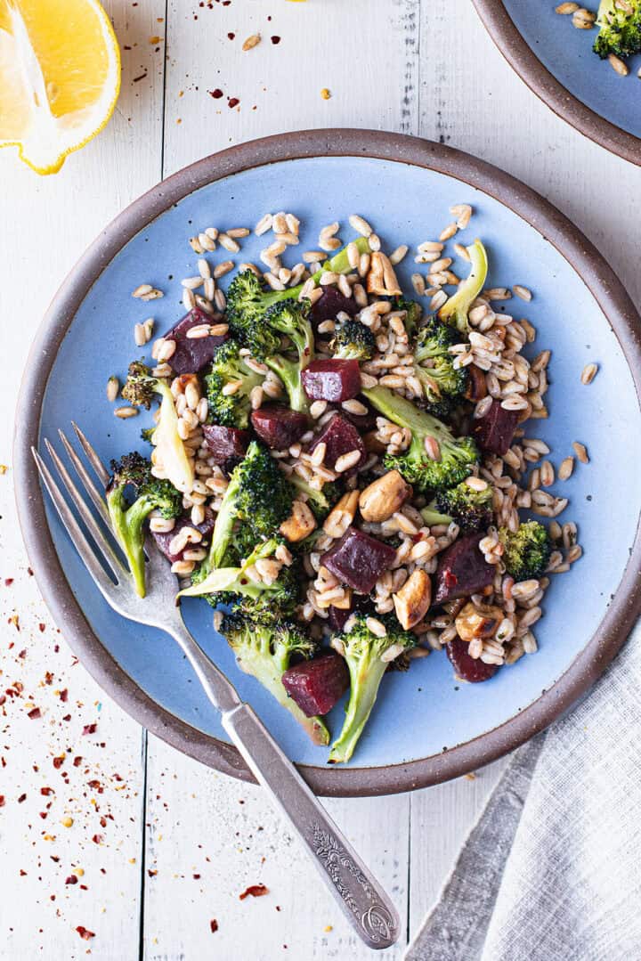 broccoli salad served on blue plate with fork, grey napkin