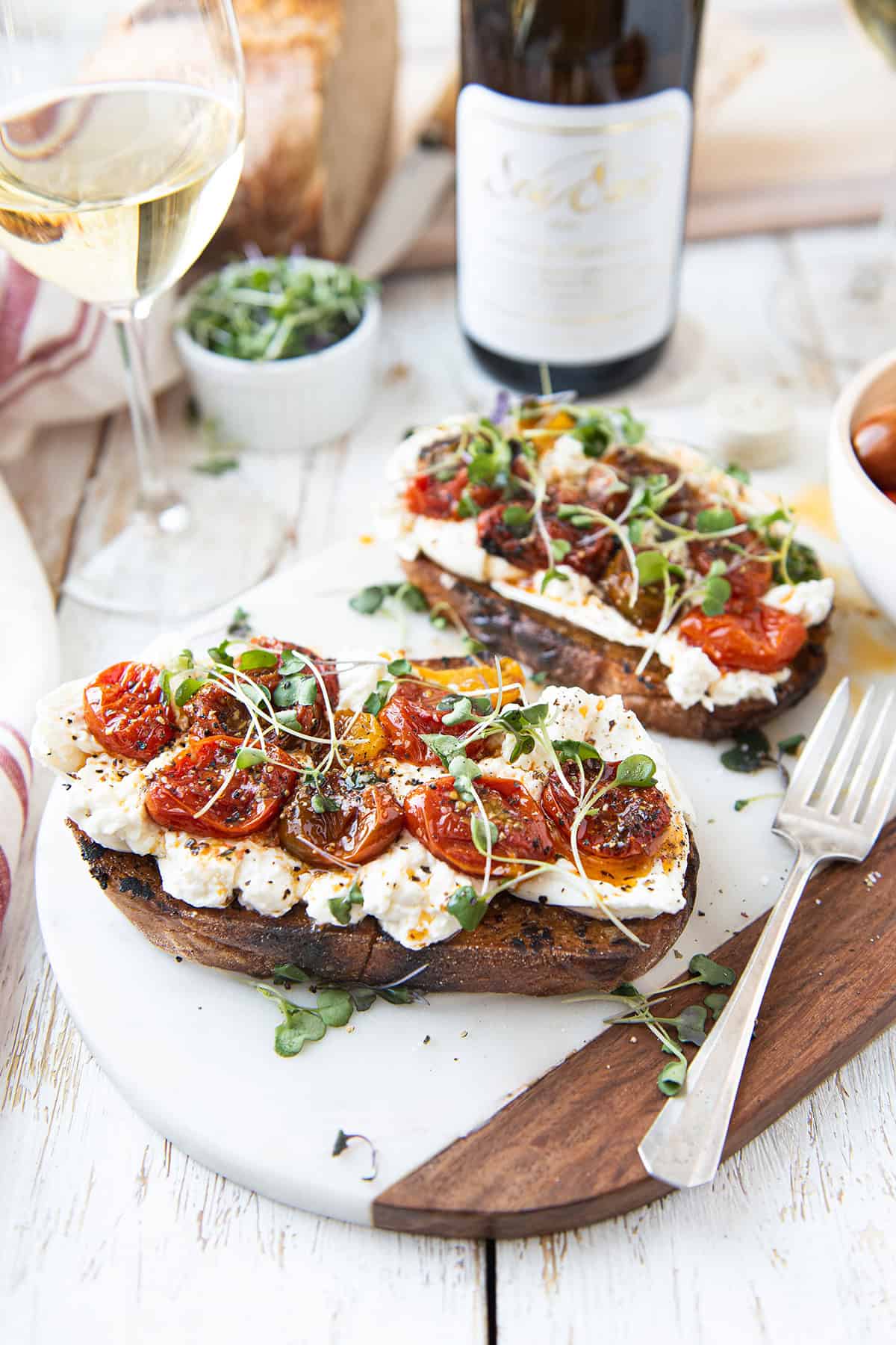 Burrata sourdough toast with roasted cherry tomatoes and micro greens served alongside a glass of white wine