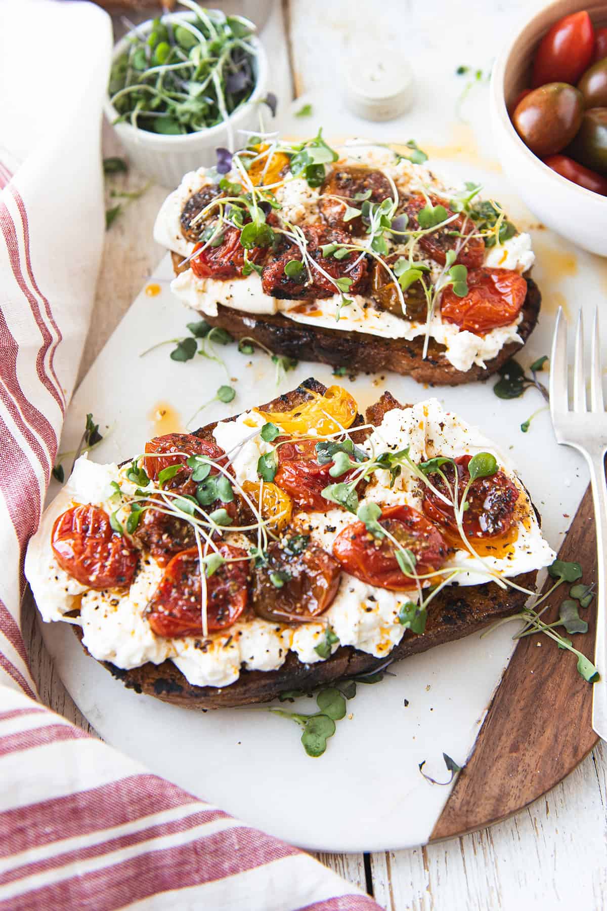 Close up overhead view of burrata toast topped with blistered mixed cherry tomatoes and micro greens on toasted sourdough